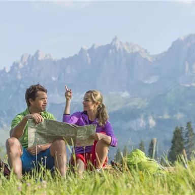 Ein Paar sitzt im Grünen und studiert eine Karte. Im Hintergrund sind majestätische Berge zu sehen.