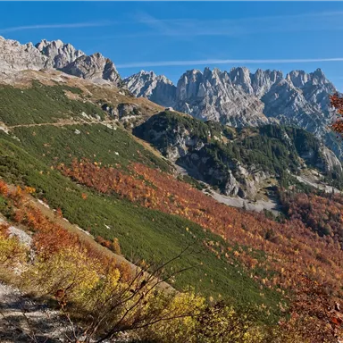 An autumn mountain landscape with colorful foliage and steep rocks. The clear blue sky complements the stunning view.