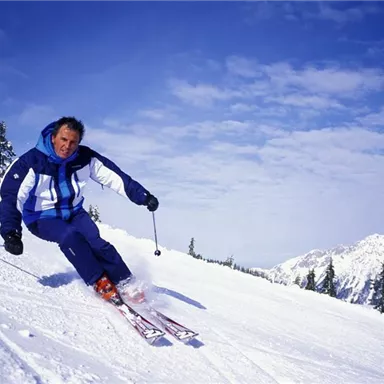 A skier gracefully descends the snow-covered slope. In the background, there are snow-covered mountains and a clear sky.