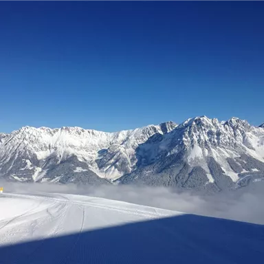 A majestic mountain range with snow-capped peaks under a clear blue sky. The snowy landscape radiates tranquility and cold.