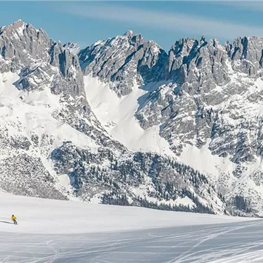 A snowy landscape with majestic mountains in the background. Two skiers glide over the glistening snow.
