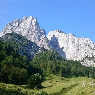 An impressive mountain massif with steep cliffs and lush green in the foreground. The clear blue sky complements the picturesque landscape.
