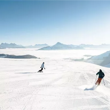 A sunny day on the ski slope with three skiers. The untouched, snow-covered landscape extends to the horizon.