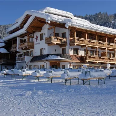 A cozy hotel in a snowy landscape. The snow rests on the roof and in the surroundings, while the trees in the background are visible.