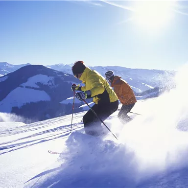 Two skiers glide over a snow-covered slope in the mountains. The sun shines in the clear sky.