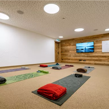 A bright, quiet room with yoga mats in different colors. There is a television on the wall and the atmosphere is calming.