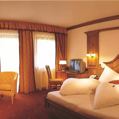 A cozy hotel room with a large bed and colorful curtains. There is a seating area with a table and a television in the room.