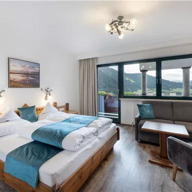 A cozy hotel room with a large bed, a sitting area, and windows that offer a beautiful view of the mountains. The decor is modern and inviting.