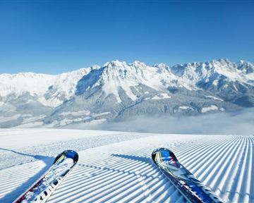 Ein atemberaubender Blick auf schneebedeckte Berge und perfekte Pisten. Die Sonne scheint am klaren blauen Himmel, ideal für Skifahrer.