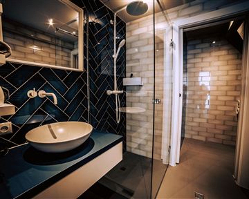 A modern bathroom with blue tiles and an elegant sink. There is a glass shower cabin and a bright, inviting atmosphere.