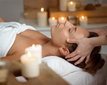 A relaxing wellness treatment with a woman receiving a head massage. The surroundings feature candles and a tranquil atmosphere.