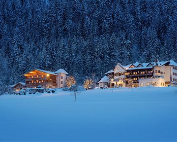 A wintry landscape with snow-covered hills. Cozy houses gently glow in the twilight.