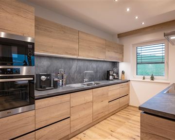 Eine moderne Küche mit Holzmöbeln und grauem Arbeitsblatt. Sie ist hell und gut ausgestattet mit modernen Geräten.