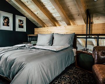 Ein modernes Schlafzimmer mit einem großen Bett und grauer Bettwäsche. Die Holzbalken und die stilvolle Einrichtung schaffen eine gemütliche Atmosphäre.