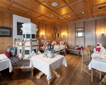 Ein gemütliches Restaurant mit Holzwänden und elegant eingedeckten Tischen. In der Mitte steht ein traditioneller Kachelofen.