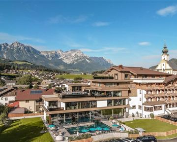 Ein modernes Hotel mit einem Schwimmbad und einer schönen Aussicht auf die Berge. Die Umgebung ist grün und idyllisch, ideal für einen entspannten Urlaub.