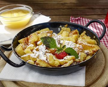 A delicious Kaiserschmarrn, served in a pan, with powdered sugar, fresh berries, and mint. Accompanied by a bowl of applesauce.