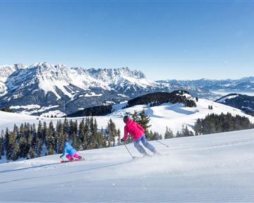 Ein schönes Wintersportgebiet mit schneebedeckten Pisten und Bergen im Hintergrund. Zwei Skifahrer genießen die Sonne und die frische Luft.