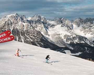 Two skiers are skiing down the snow-covered slope in the mountains. In the background, majestic mountain peaks can be seen.