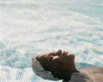 Ein Mann liegt entspannt auf dem Wasser in einem Pool. Die sanften Wellen spiegeln das Licht wider und schaffen eine ruhige Atmosphäre.