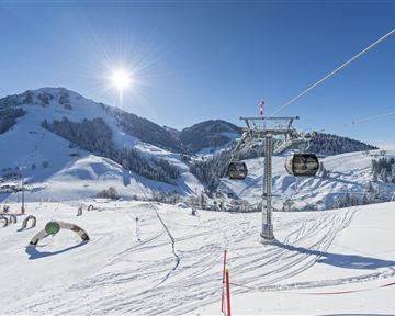 Eine idyllische Winterlandschaft mit skifahrenden Hängen und einem Sessellift. Der Himmel ist klar und die Sonne strahlt über den schneebedeckten Bergen.