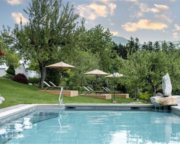 Ein schöner Pool inmitten einer grünen Landschaft mit Bäumen. Liegestühle und Sonnenschirme runden die entspannende Atmosphäre ab.