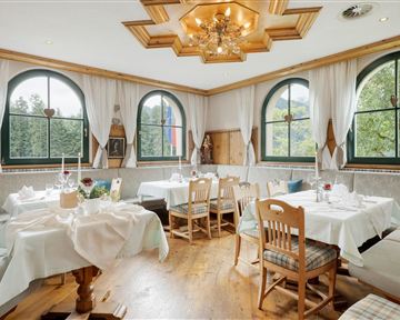 A cozy restaurant with elegant tables and chairs. Large windows offer a beautiful view of the green surroundings.