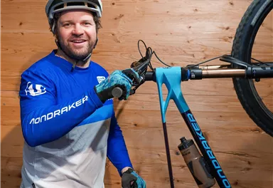Ein Mann steht neben einem Mountainbike und lächelt. Er trägt einen Helm und sportliche Kleidung in Blau und Weiß.