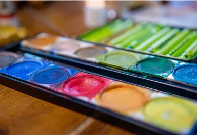 Eine Palette mit Wasserfarben in verschiedenen Farben liegt auf einem Tisch. Die Farben sind ordentlich angeordnet und strahlen Kreativität aus.