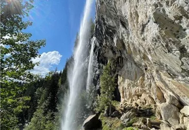 Ein schöner Wasserfall, der die Felsen hinunterstürzt, umgeben von grünen Pflanzen und Bäumen. Der Himmel ist klar und die Sonne scheint strahlend.