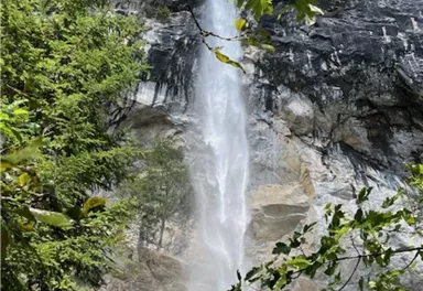 Ein beeindruckender Wasserfall, der aus hohen Felsen herausstürzt. Umgeben von grünen Bäumen und strahlend blauem Himmel.