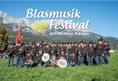 Eine Gruppe von Musikern in traditioneller Kleidung steht auf einer Wiese. Im Hintergrund sind Berge und ein klarer Himmel zu sehen.