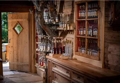 A cozy interior with wooden paneling and a shelf full of bottles. An open door lets light in and creates an inviting atmosphere.