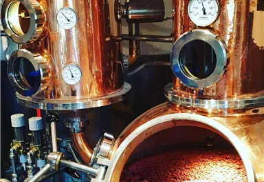 A copper still with measuring instruments and a large container holding a red liquid. The place looks professional and industrial.