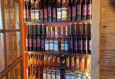 Ein Holzregal mit vielen Flaschen verschiedener Weine und Liköre. Die Flaschen sind gut sortiert und farbenfroh etikettiert.