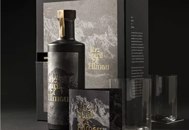 Ein elegantes Geschenkset mit einer Flasche und Gläsern. Die Verpackung hat ein modernes Design mit einem Bergmotiv und der Aufschrift „the spirit of Elmnau“.