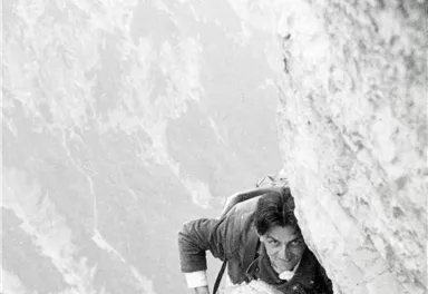 Ein kletternder Mann an einer steilen Felswand. Er scheint sich in einer herausfordernden Position zu befinden.