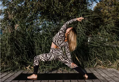 Eine Frau macht Yoga in einer Wildnisumgebung. Sie trägt ein gestreiftes Outfit und steht auf einer Matte.