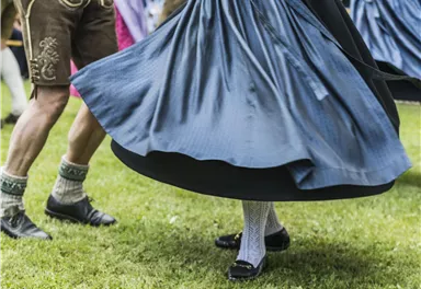 Tänzer in traditionellen Trachten zeigen einen fröhlichen Tanz im Freien. Der weite Rock einer Tänzerin schwingt elegant in der Luft.