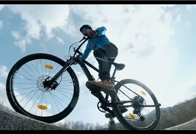 Ein Mountainbiker fährt auf einem schmalen Weg. Der Himmel ist teilweise bewölkt und der Biker zeigt eine dynamische Fahrhaltung.