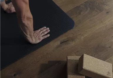 Eine Person macht eine Übung auf einer Yogamatte. Neben ihr liegen Korkblöcke auf einem Holzboden.