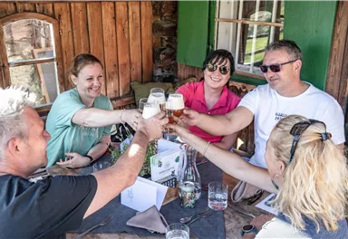 Eine Gruppe von Freunden stößt mit Gläsern an. Sie sitzen an einem Holztisch in einer gemütlichen Umgebung.