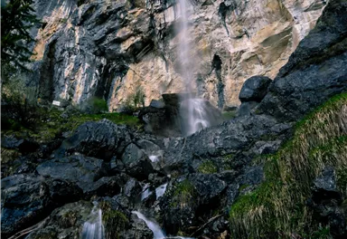 Ein wunderschöner Wasserfall fließt von steilen Felsen in einen klaren Pool. Umgeben von üppigem Grün und deinem steinigen Gelände.