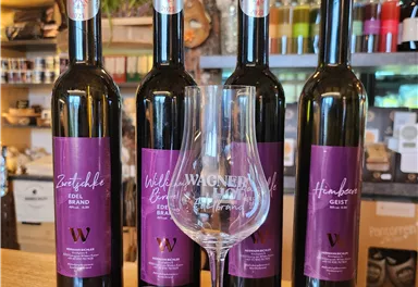Four bottles of wine with elegant labels stand on a wooden shelf, accompanied by a wine glass. The bottles are labeled in different varieties, giving the ambiance an inviting atmosphere.