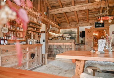 Ein gemütliches Holzinterieur mit einer einladenden Theke. Regale sind mit Flaschen und Gläsern gefüllt, und der Raum strahlt eine warme Atmosphäre aus.