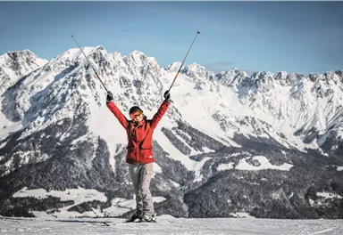 Eine fröhliche Person steht auf Skiern in der winterlichen Berglandschaft. Im Hintergrund sind majestätische, schneebedeckte Berge zu sehen.