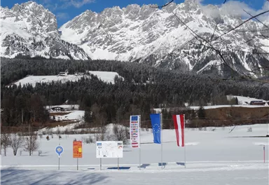 Eine verschneite Landschaft mit majestätischen Bergen im Hintergrund. Mehrere Fahnen und Schilder stehen im Vordergrund.