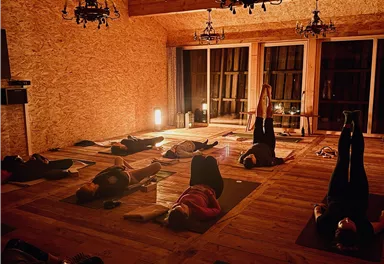 Ein dunkler Raum mit Menschen, die auf Yogamatten liegen und meditieren. Die Atmosphäre ist ruhig, beleuchtet von sanftem Licht und Kronleuchtern.