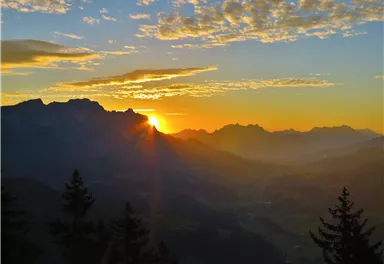 Ein beeindruckender Sonnenaufgang über den Bergen. Die Sonne strahlt durch die Wolken und farbenfrohe Lichtspiele erleuchten die Landschaft.