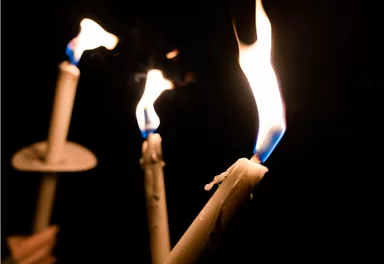 Drei brennende Kerzen in der Dunkelheit. Die Flammen leuchten warm und flackern sanft.